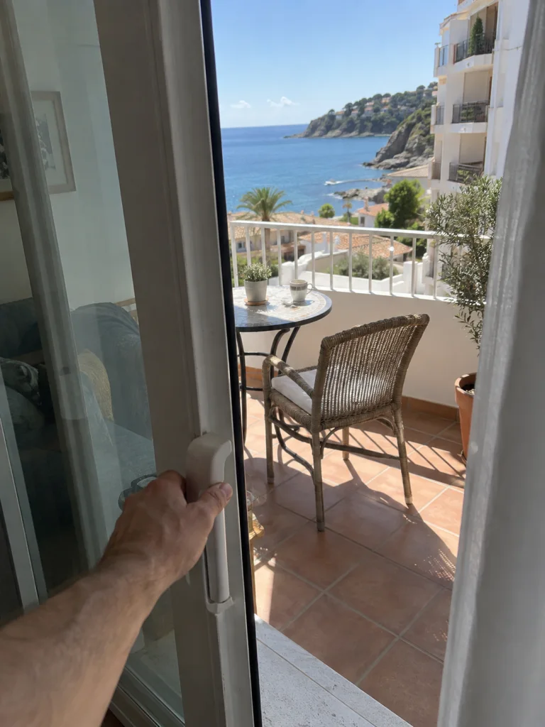 Vista en primera persona de una mano que abre la puerta de una terraza frente al mar.